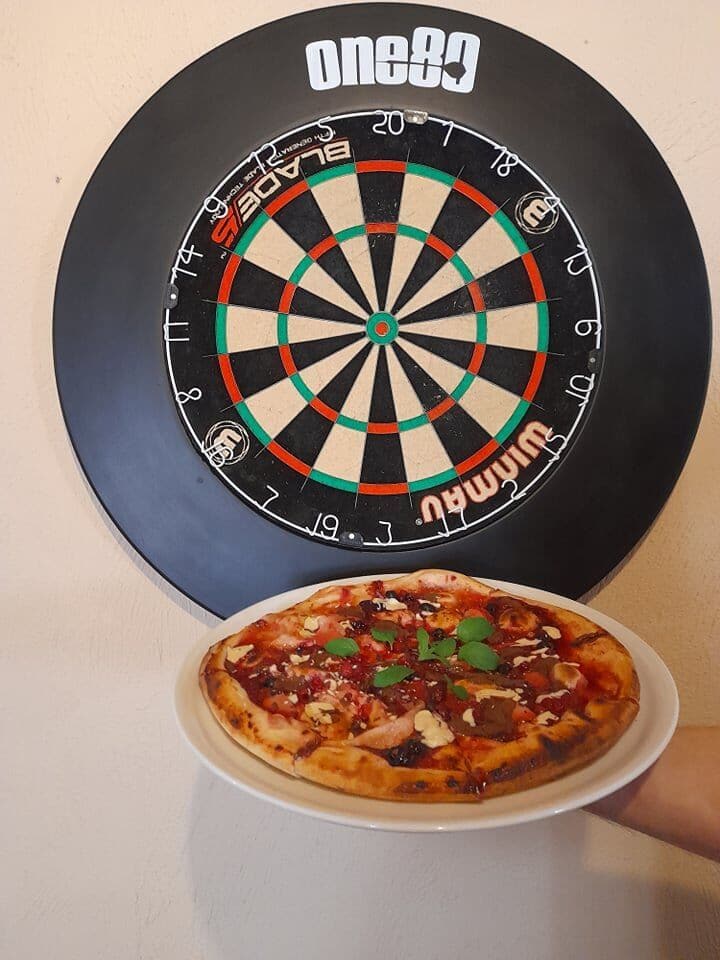 Pizza servírovaná pred elektronickým šípkovým terčom